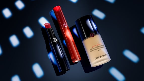 Main de femme tenant des produits de maquillage, dont un fond de teint, un rouge à lèvres et un vernis à ongles.